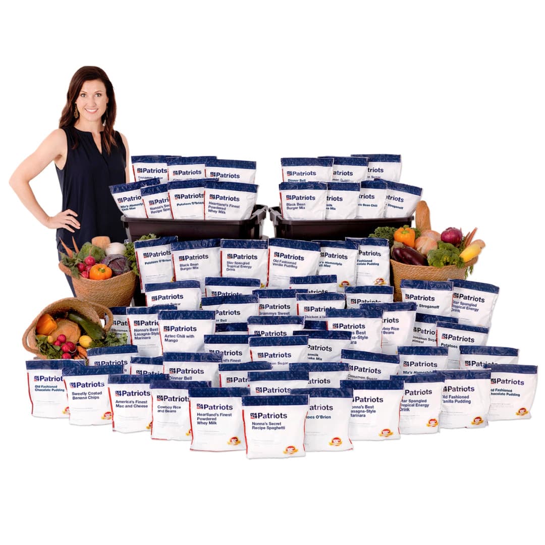 Large assortment of food packages from 4Patriots 3-Month Emergency Survival Food Kit neatly arranged in front of included stacked black storage totes. A smiling woman stands to the left, by a basket of fresh vegetables.